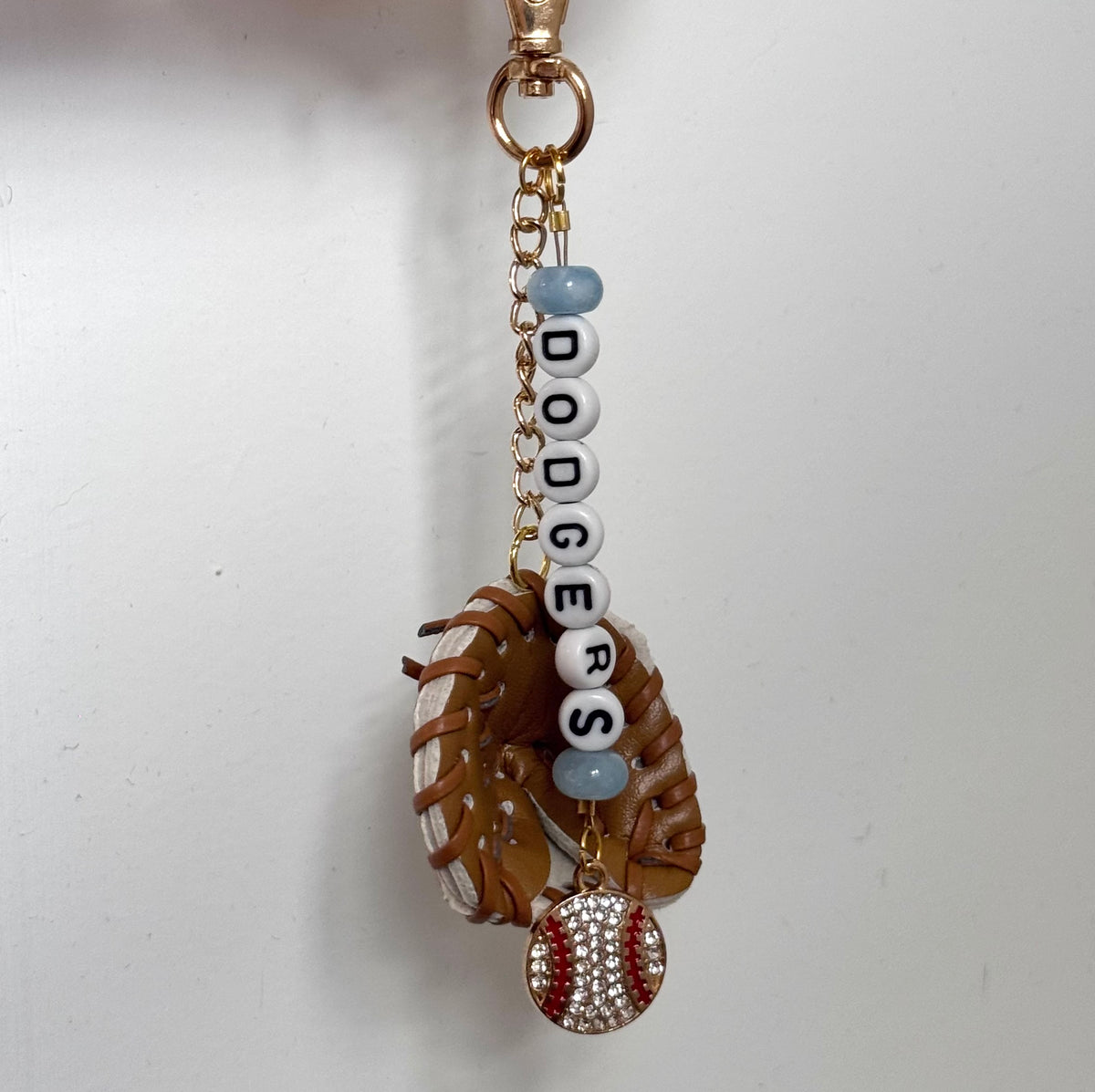 A baseball-themed keychain charm featuring a brown glove, a baseball with rhinestone detailing, and white letter beads spelling 'DODGERS' with light blue beads.